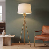 Lámpara de pie trípode TRINA GOLD dorada encendida en sala con muro verde salvia