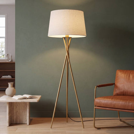 Lámpara de pie trípode TRINA GOLD dorada encendida en sala con muro verde salvia