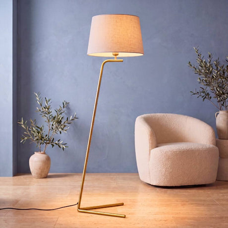 Lámpara de pie VERA GOLD dorada encendida junto a butaca bouclé en sala moderna