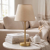 Lámpara decorativa NORA GOLD dorada sobre mantas de lino dobladas