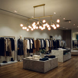 Iluminacion de realce para boutique de ropa con lampara colgante dorada lineal.