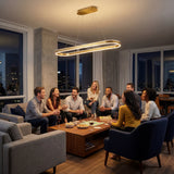 Grupo de personas conversando en una sala iluminada por la lámpara colgante ovalada de luz cálida.