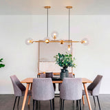 Lámpara de esferas dorada Amber Line instalada sobre una elegante mesa de comedor de 6 sillas.