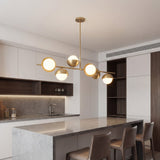 Lampara lineal Nova Gold instalada sobre una isla de cocina moderna con encimeras de marmol.
