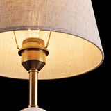 Detalle de la pantalla de tela encendida de la lámpara de mesa Olivia Gold sobre fondo oscuro