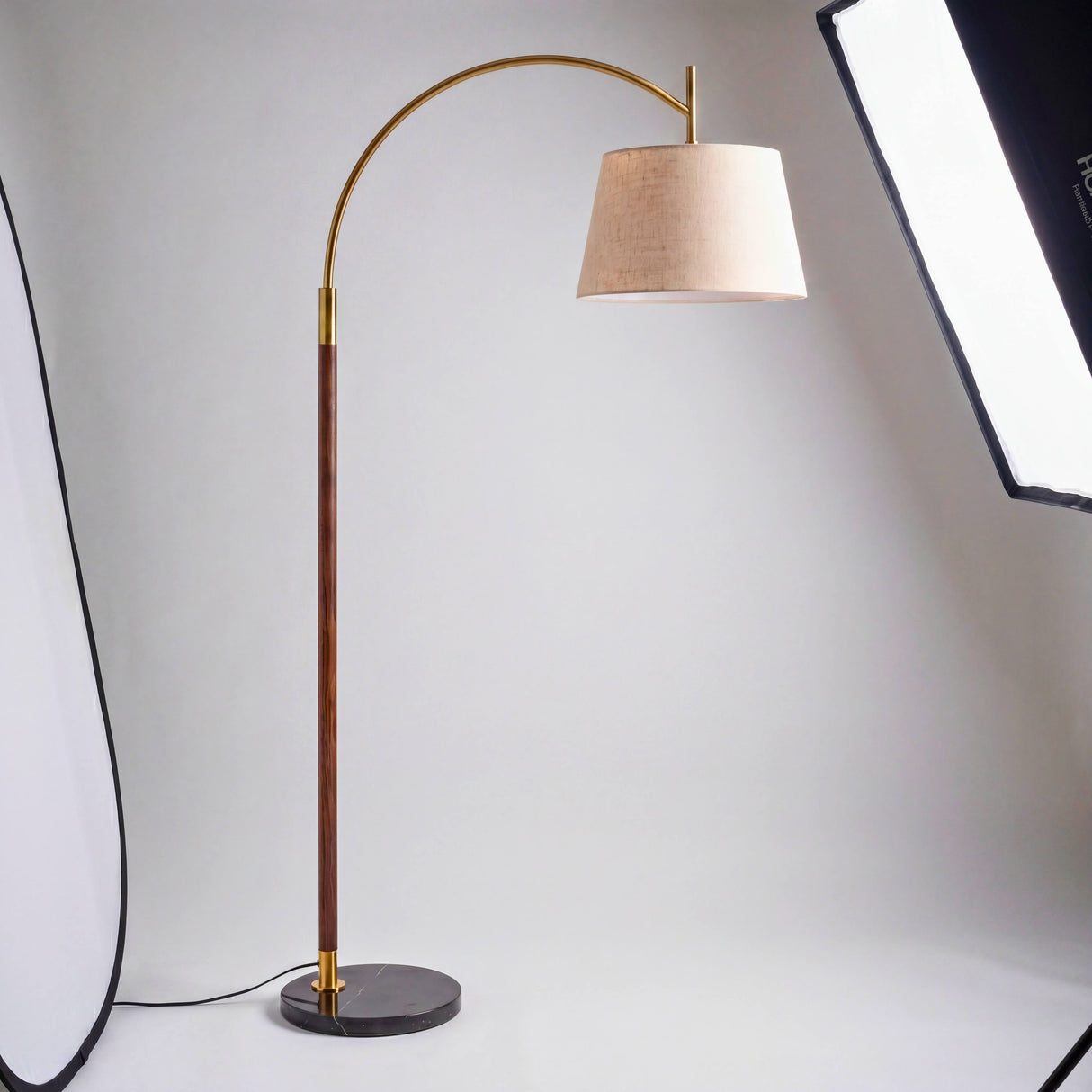 Toma lateral en estudio fotográfico de luminaria minimalista con arco de acero dorado.
