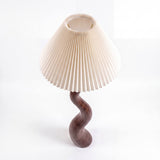 Lámpara de sobremesa con base curva de madera y pantalla plisada para iluminación de acento.