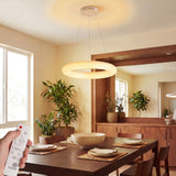Luminaria LED circular minimalista blanca sobre mesa de comedor con control remoto en primer plano.