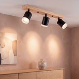 Lámpara de techo BRISA con base de madera y 3 spots negros iluminando un muro nude