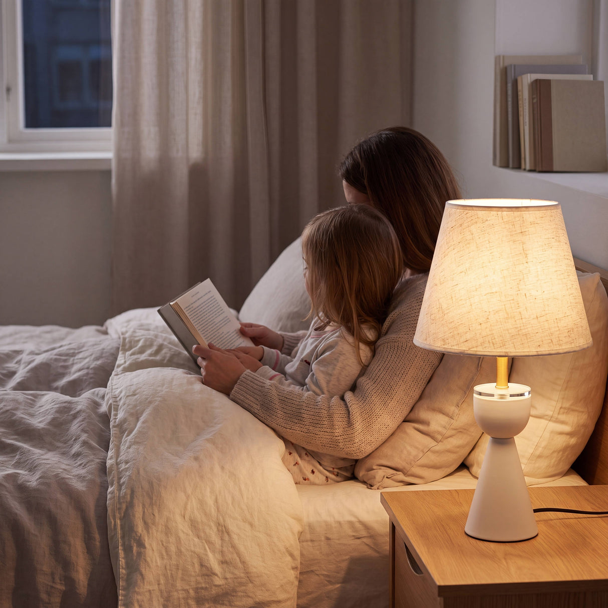 Lámpara de velador BIANCA encendida iluminando momento de lectura en dormitorio