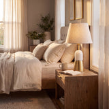 Lámpara de velador dorada sobre mesa de noche en dormitorio con decoración cálida