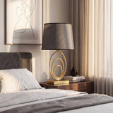 Lámpara de velador dorada sobre mesa de noche junto a la cama