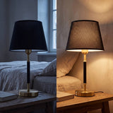 Lámpara de velador negra y dorada sobre mesa de noche junto a la cama