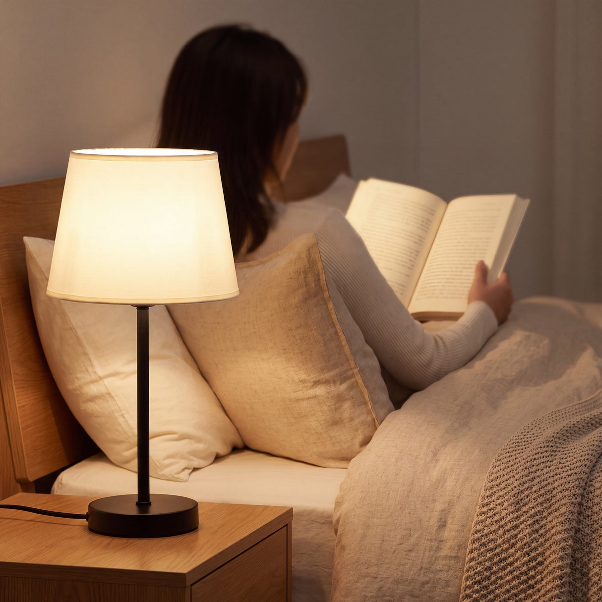 Lámpara de velador NORA iluminando lectura nocturna en dormitorio acogedor
