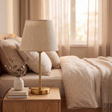 Lámpara de velador NORA GOLD sobre mesa de noche en dormitorio con luz natural