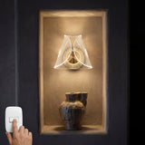 Lámpara de pared Pyramid Gold instalada en un nicho iluminando un jarrón decorativo con luz cálida.