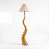 Diseño minimalista de luminaria de pie en madera con silueta fluida inspirada en la naturaleza para interiorismo.