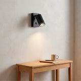 Iluminación ambiental cálida sobre mesa auxiliar en rincón de lectura con luminaria negra.
