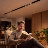Hombre leyendo en sillón bajo la luz cálida del spot para riel magnético