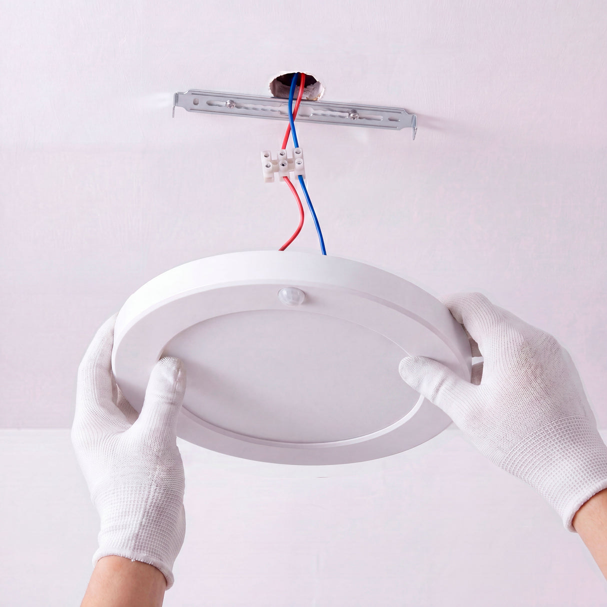 Técnico calificado instalando plafón directamente en el punto de alimentación cenital con guantes.