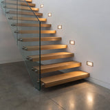 Guía lumínica para escaleras de diseño con barandillas de cristal y madera.
