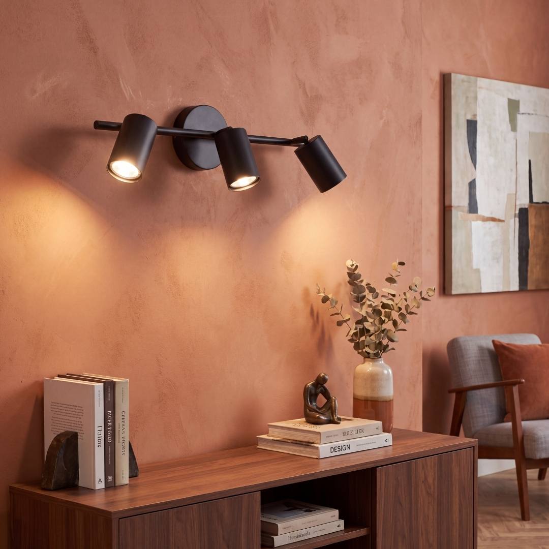Spot triple negro iluminando repisa decorativa con luz cálida
