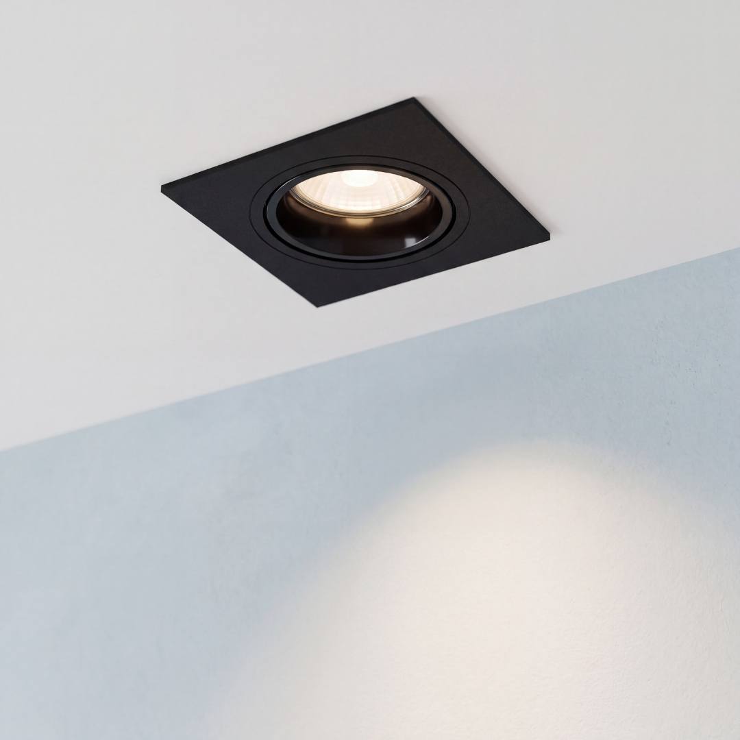 Spot empotrable cuadrado LEA negro encendido en techo blanco con luz cálida sobre muro celeste
