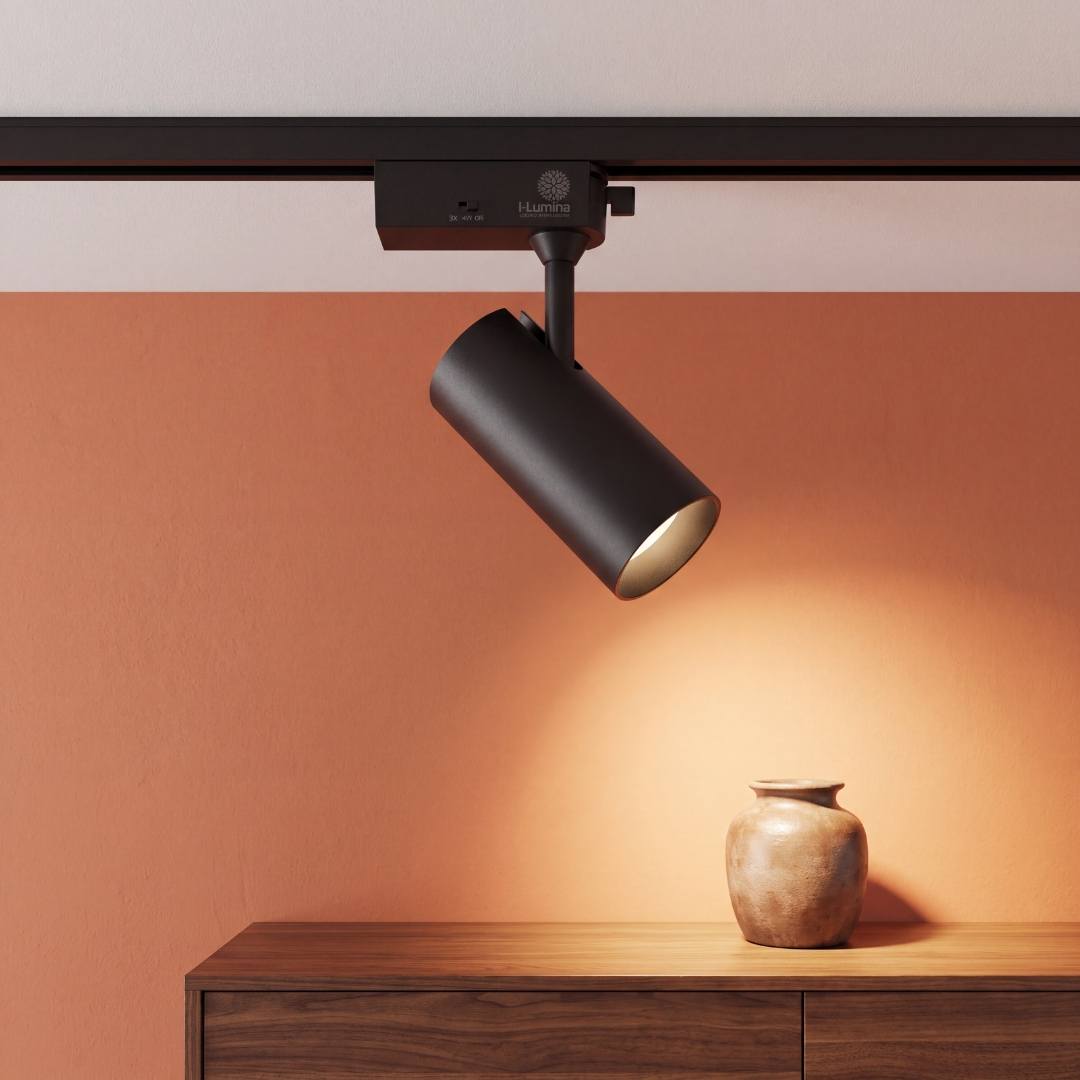 Spot LED para riel TRIXY Black encendido iluminando un jarrón en muro naranja